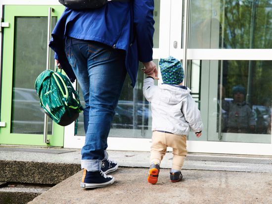 Ein Kind und seine Mutter gehen zum Eingang einer Kita. 