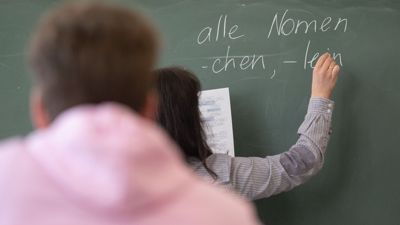 Eine Lehrerin schreibt im Unterricht an die Tafel.