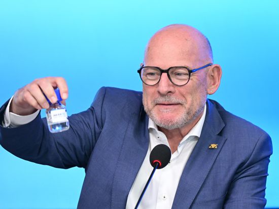 Winfried Hermann hält bei einer Regierungs-Pressekonferenz im Landtag eine Flasche mit reFuels in der Hand.