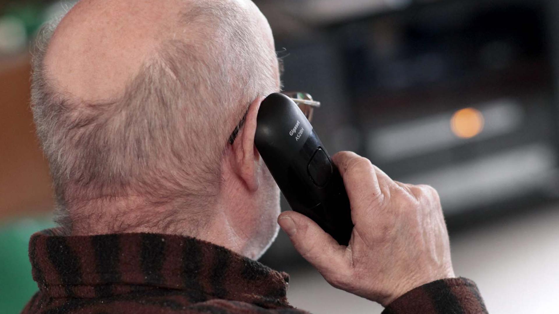 Ein Senior hält ein Telefon am Ohr. 
