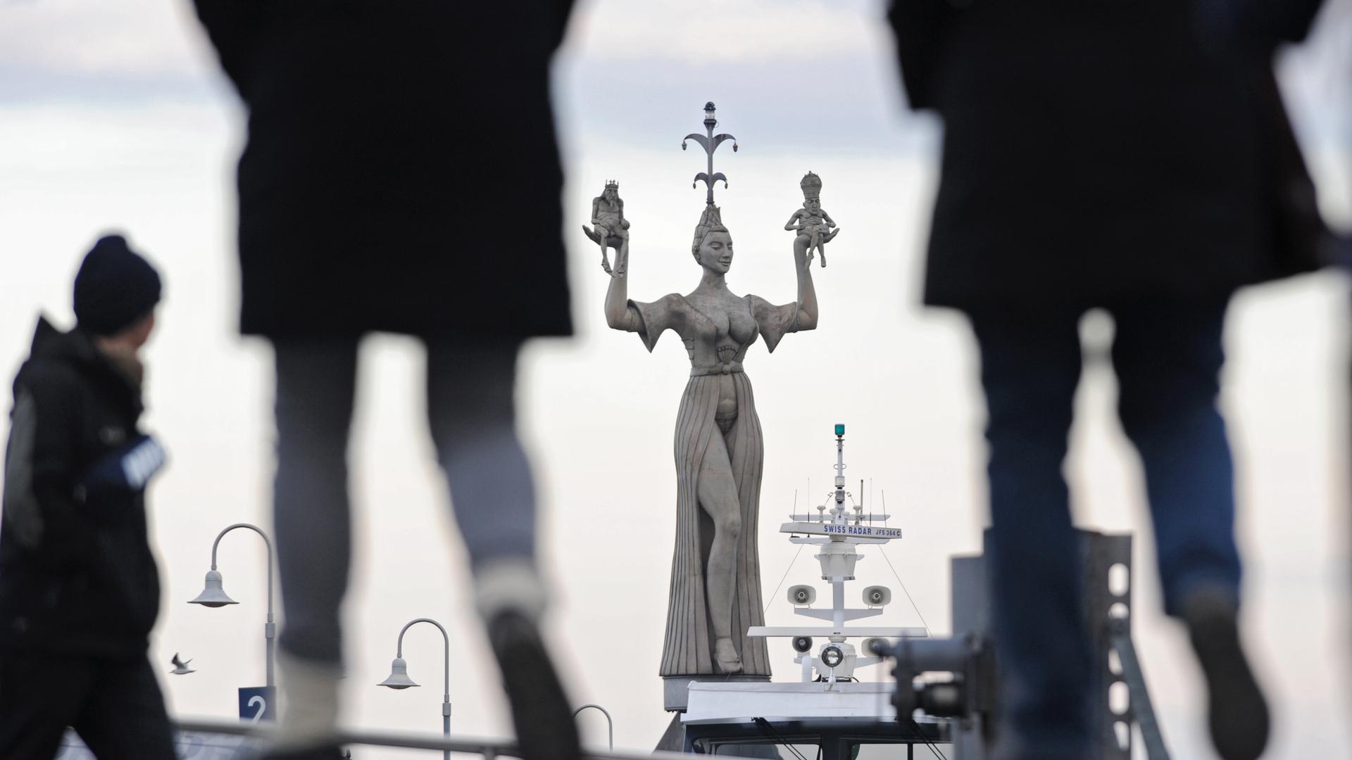 Zwei Frauen laufen in Konstanz am Bodensee auf die vom Künstler Peter Lenk entworfene Hafenstatue Imperia zu. 