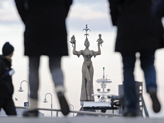 Zwei Frauen laufen in Konstanz am Bodensee auf die vom Künstler Peter Lenk entworfene Hafenstatue Imperia zu. 