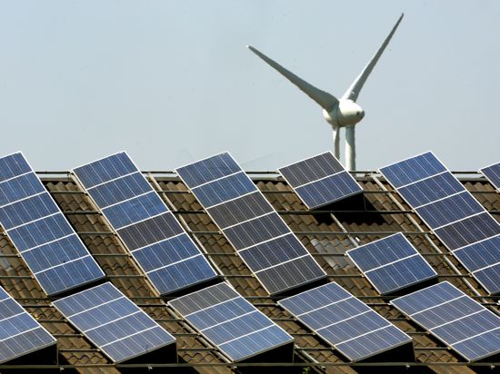 Hinter den Photovoltaik-Panelen auf einem Scheunendach dreht sich eine Windkraftanlage.