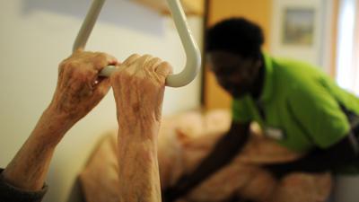 Eine Pflegehelferin hilft in einem Seniorenzentrum einer Pflegehausbewohnerin, sich hinzulegen.
