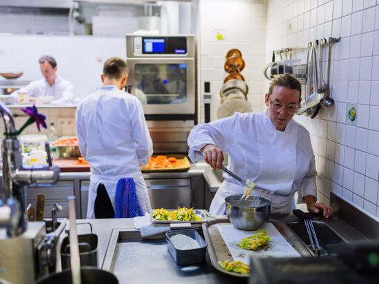 Ein Koch und eine Köchin  stehen in der Küche eines Restaurants und bereiten den abendlichen Betrieb vor. 