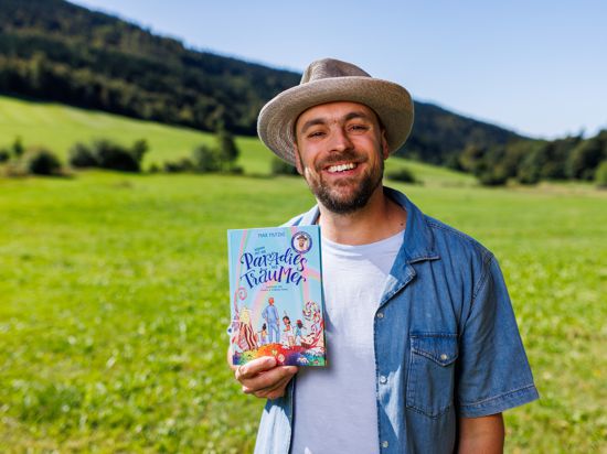 Max Mutzke steht nahe Herrenschwand im Schwarzwald und hält sein Kinderbuch „Komm mit ins Paradies der Träumer“ in der Hand. 