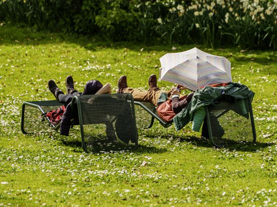 Ein Besucher eines Parks schützt sich mit einem Schirm auf der Liegewiese vor der Sonne. 