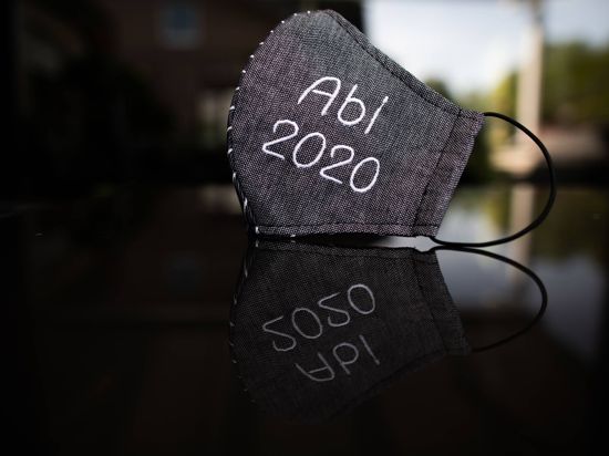Corona-Schutzmaske mit aufgesticktem Schriftzug „Abi 2020” liegt auf einem Tisch.
