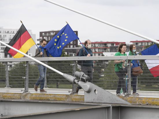 14.06.2020, Frankreich, Straßburg: Mitglieder pro-europäischer französischer und deutscher Verbände gehen mit der deutschen, französischen und europäischen Fahne auf der «Passerelle des Deux-Rives» (Fußgängerbrücke der beiden Ufer), die das französische Straßburg mit dem deutschen Ort Kehl (Baden-Württemberg) verbindet. Die Bundesregierung hebt ab dem 15. Juni für 27 EU-Staaten die Reisewarnung wieder auf, darunter auch für Frankreich. Foto: Jean-Francois Badias/AP/dpa +++ dpa-Bildfunk +++ |