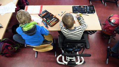 Ein Kind mit Behinderung sitzt in seinem Rollstuhl gemeinsam mit einem Erstklässler ohne Handicap in einem Klassenraum. 