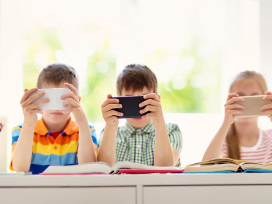 Children sitting in the room with smart phones. Pupils surfing at school