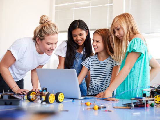 Three Female Students With Teacher Building Robot Vehicle In After School Computer Coding Class