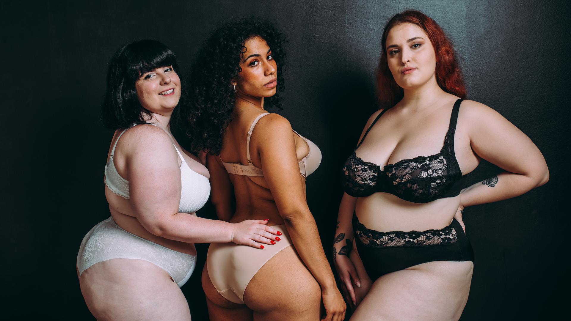 Drei mehrgewichtige Frauen schauen für ein Fotoprojekt selbstbewusst in die Kamera. 