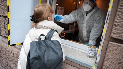 Eine Mitarbeiterin führt an einer Teststation, die sich in einem Café befindet und in der sich Passanten durch ein Fenster testen lassen können, einen Corona-Schnelltest an einer Frau durch. 