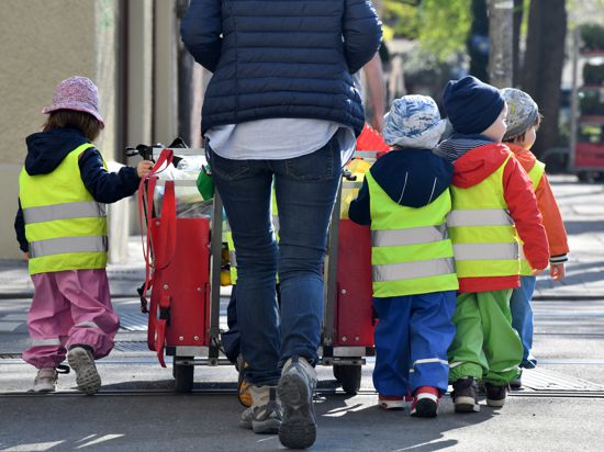Eine Betreuerin läuft mit mehreren Kleinkindern über einen Bürgersteig.