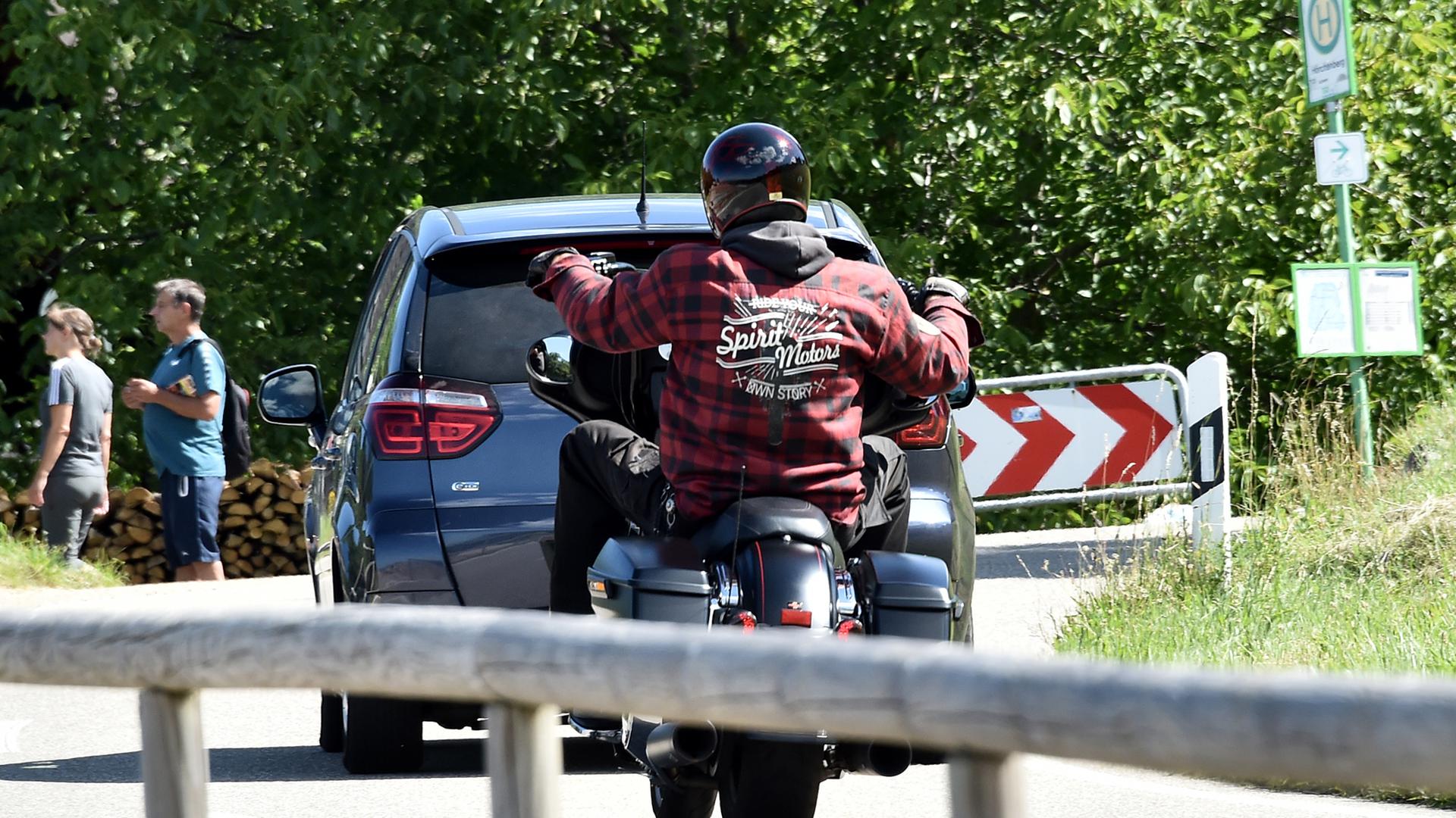 Ein Motorradfahrer fährt hinter einem Autofahrer.