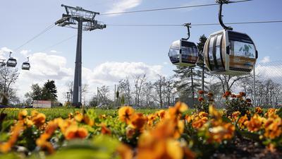 Kabinen der Seilbahn fahren auf dem Gelände der Bundesgartenschau hinter einem Blumenbeet. Die Buga beginnt am 14. April und dauert bis 8. Oktober 2023. 