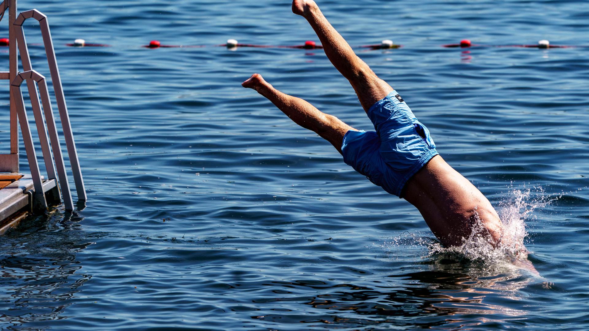 Ein junger Mann springt von einer Schwimmplattform in einen See.