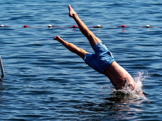 Ein junger Mann springt von einer Schwimmplattform in einen See.
