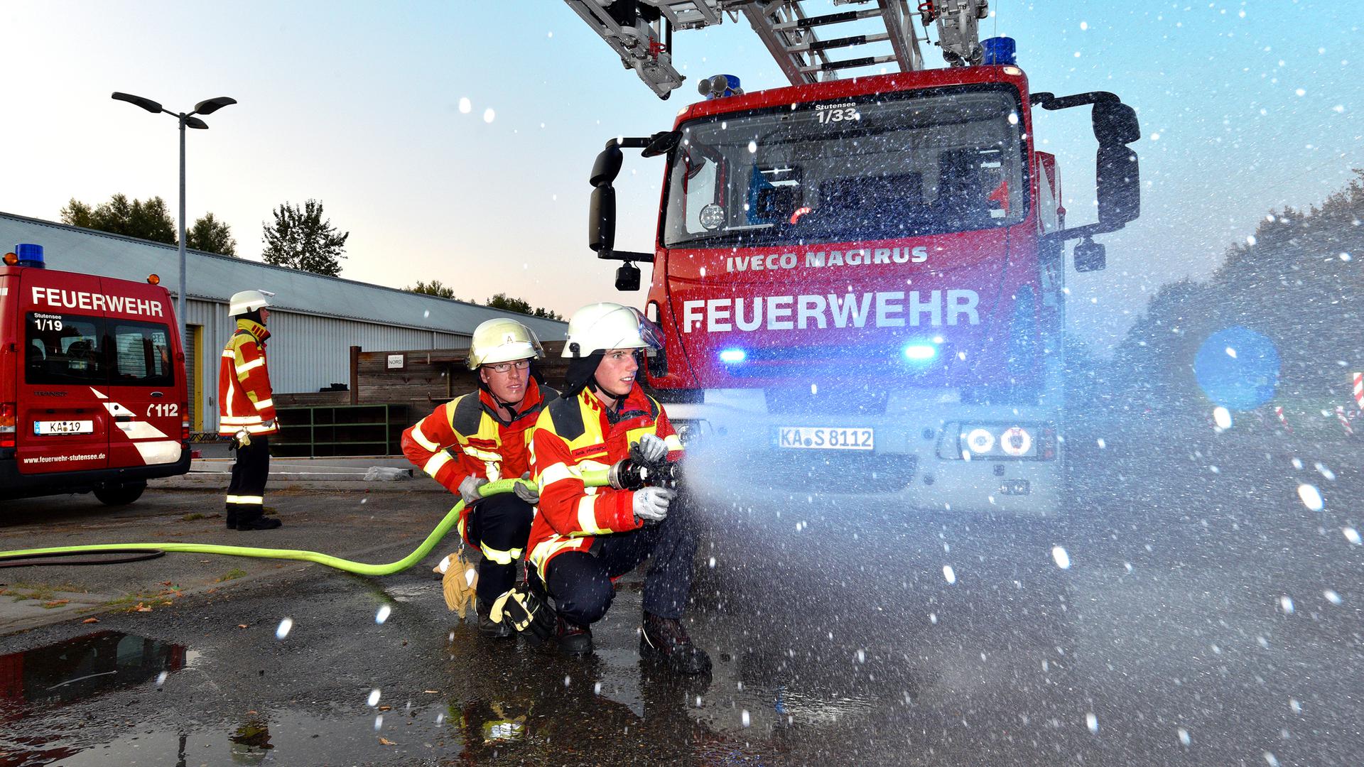 Feuerwehrkräfte halten einen Schlauch vor einem Feuerwehrauto (Symbolbild).