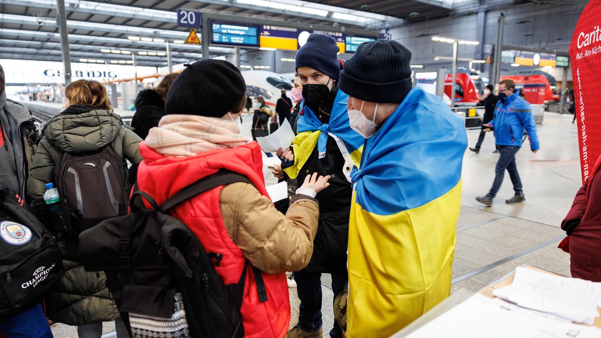 Zwei ukrainisch sprechende Helfer (rechts) sprechen an einem Info-Point am Münchner Hauptbahnhof für geflüchtete Ukrainer mit einer Frau aus der Ukraine. 