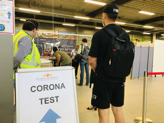 Menschen stehen vor einem kleinen und mit Stellwänden abgetrennten Bereich, in dem am Flughaen Karlsruhe/Baden-Baden kostenlose Corona-Tests erfolgen.
