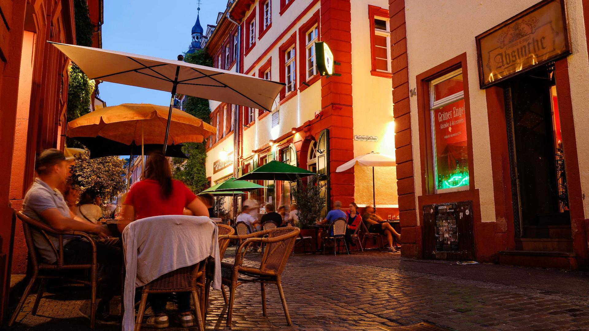 Menschen sitzen am Abend in der Innenstadt von Heidelberg vor Kneipen.