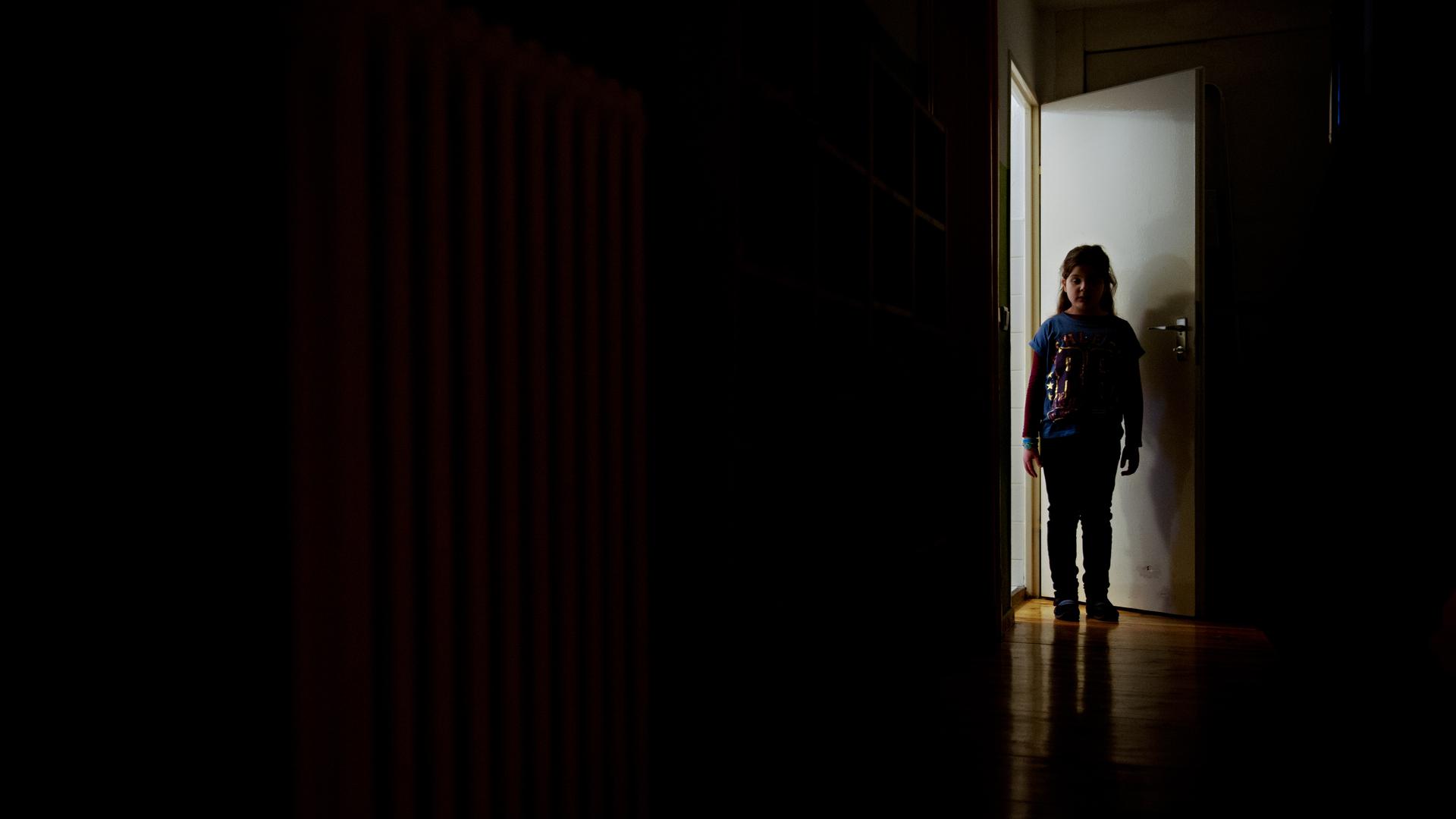 Ein junges Mädchen steht am Ende eines dunklen Flures.