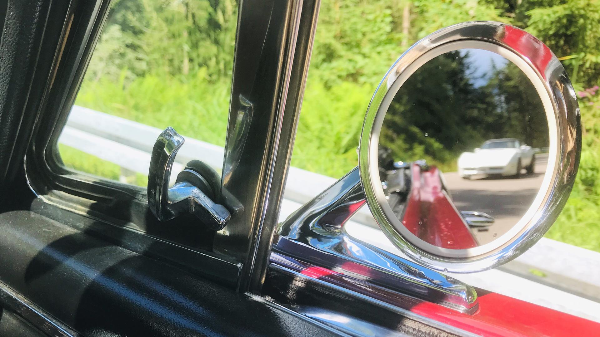 Im Außenspiegel eines Ford Mustang aus dem Jahr 1966 ist eine weiße Corvette zu sehen. 