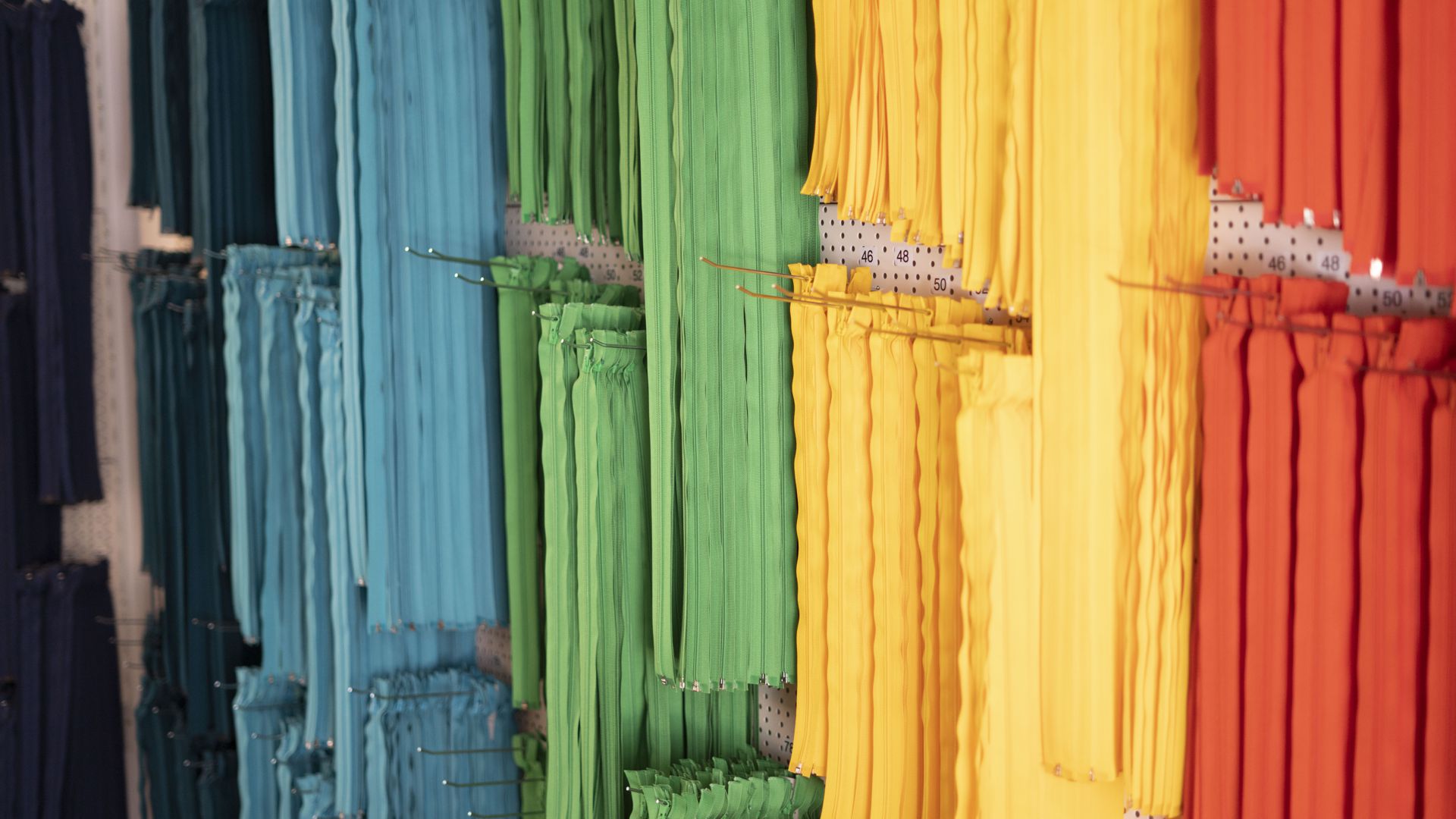 Reißverschlüsse in allen Regenbogenfarben hängen an der Wand der Schneiderei.