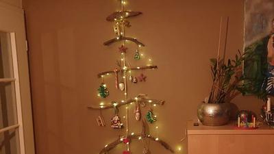 Ein Mobile aus Treibholz ist in Tannenbaumform angeordnet und mit Lichtern und Christbaumkugeln geschmückt.