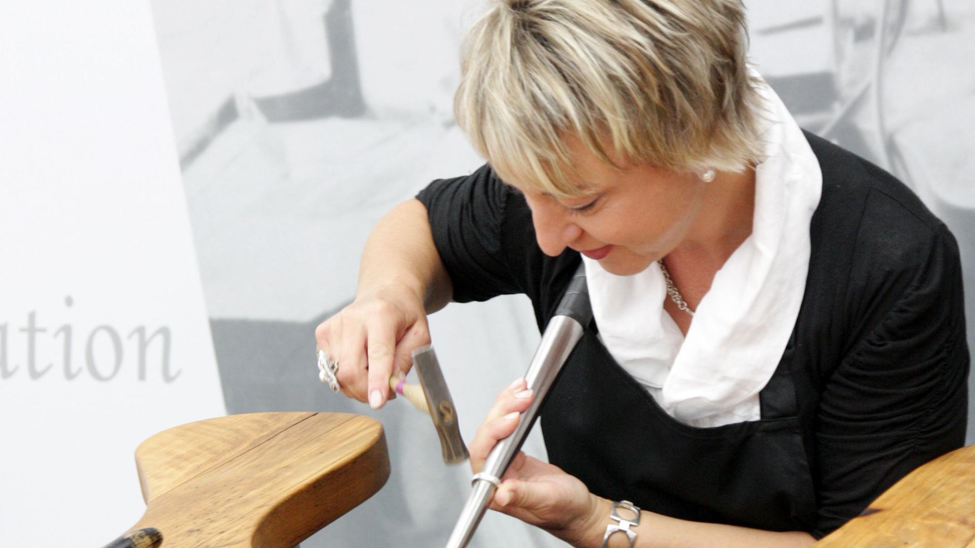 Eine blonde Frau mit kurzen Haaren arbeitet beim Schmuckworkshop an einem Silberring. 