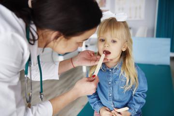 Kinderärztin untersucht kleines Mädchen, das den Mund geöffnet hat.