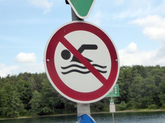Ein Schild weist an einem Gewässer auf ein Badeverbot hin.