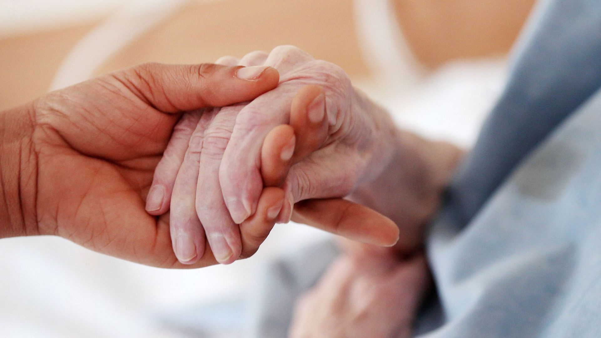 Eine Pflegerin hält in einem Altenheim die Hand einer Bewohnerin.