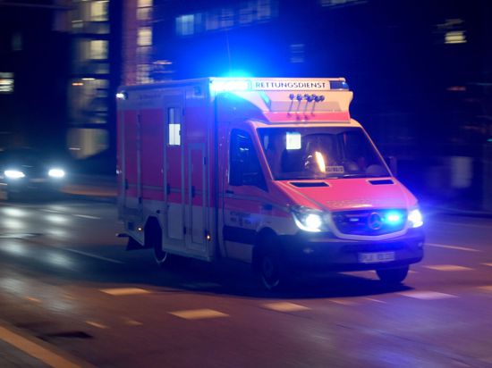 Ein Rettungswagen fährt abends mit Blaulicht über die beleuchtete Straße.