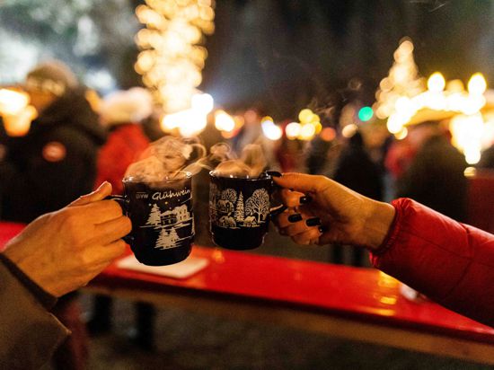 Zwei Besucherinnen stoßen in der Weihnachtszeit 2019 auf einem Weihnachtsmarkt mit Glühwein an.