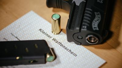 Ein Kleiner Waffenschein liegt zwischen einer Schreckschuss-Pistole und einem Magazin.