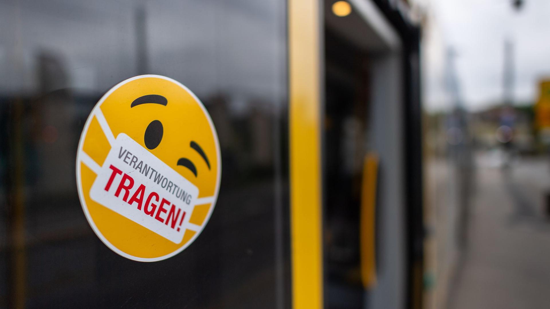 Ein Smiley-Aufkleber mit einem Mundschutz und der Aufschrift „Verantwortung tragen“ klebt an einer Scheibe einer Straßenbahn.