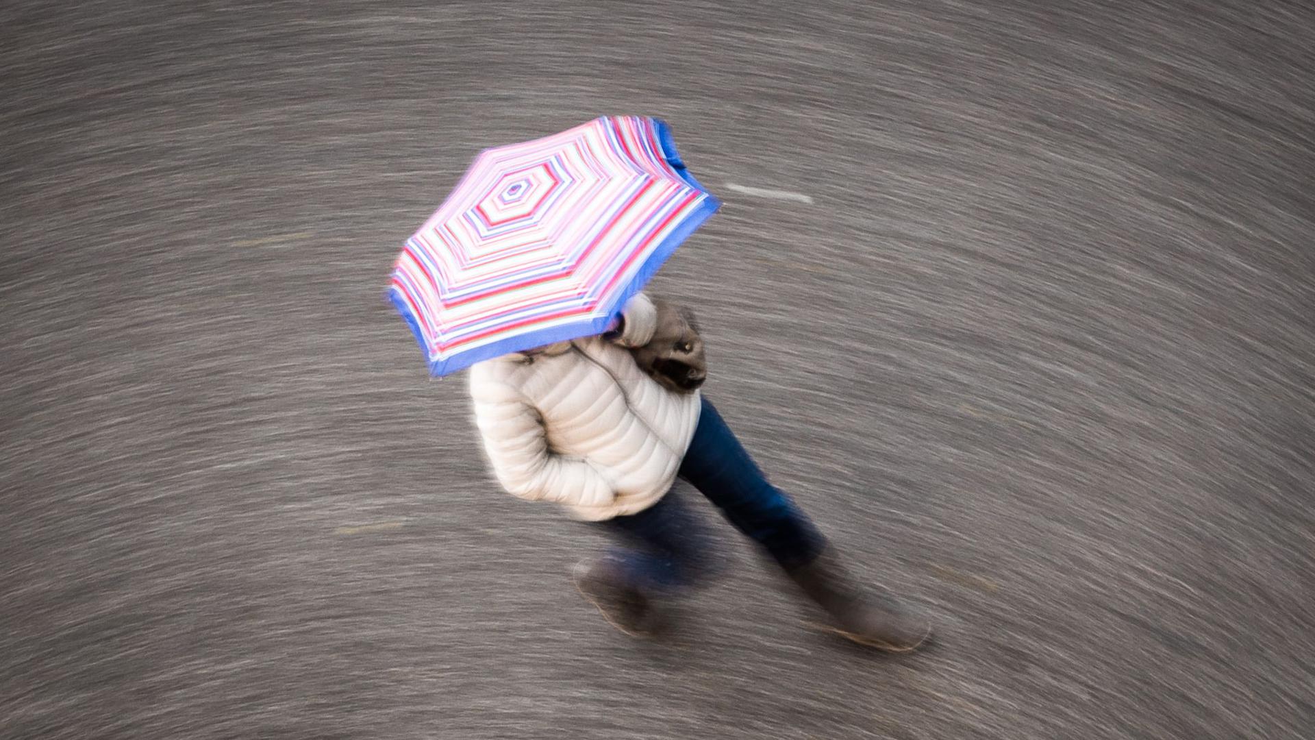 Eine Frau geht bei regnerischem Wetter über eine Straße.