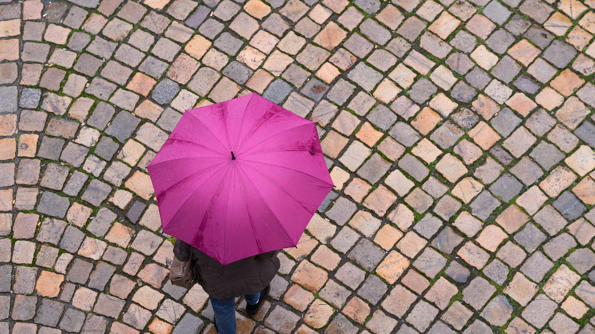 Eine Frau geht mit einem Regenschirm auf einer Straße mit Kopfsteinpflaster entlang.
