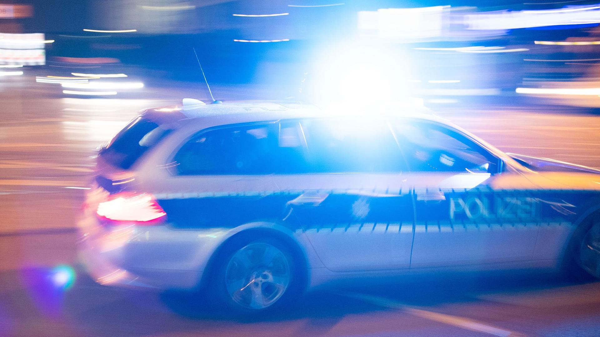 Ein Polizeiauto fährt unter Einsatz von Blaulicht und Sirene eine Straße entlang.