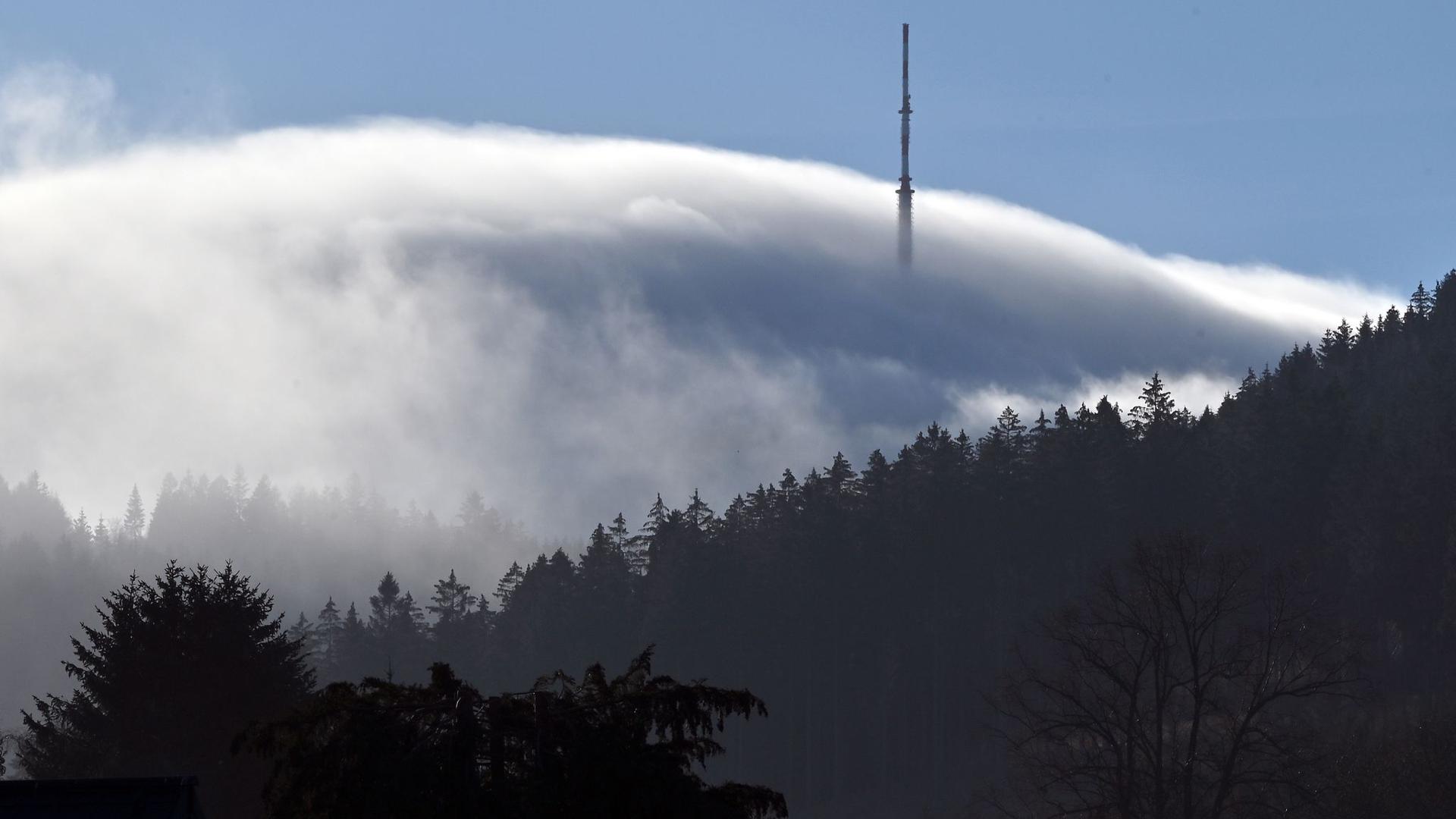 Ein Sendemast ragt an einem Hügel aus dem Nebel.