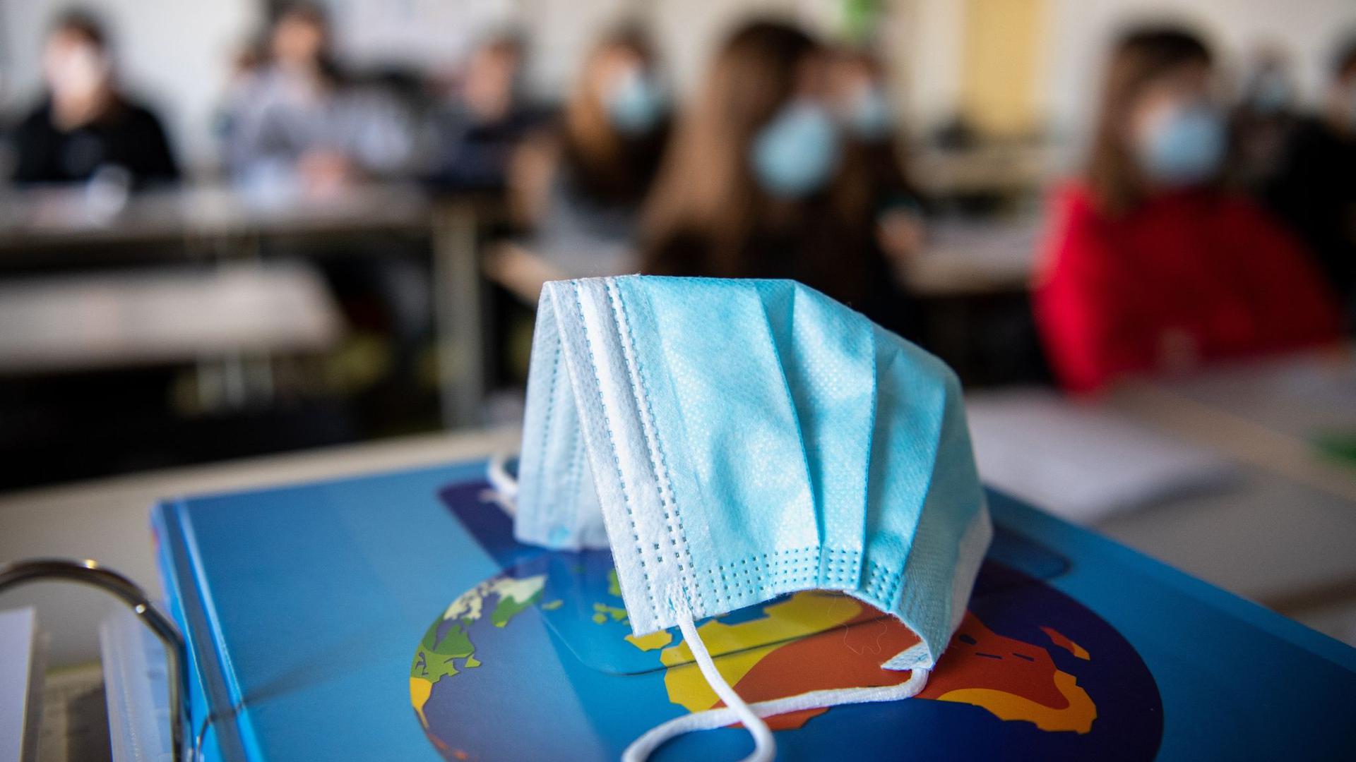 Ein Mund-Nasen-Schutz liegt während des Unterrichts auf einem Atlas.