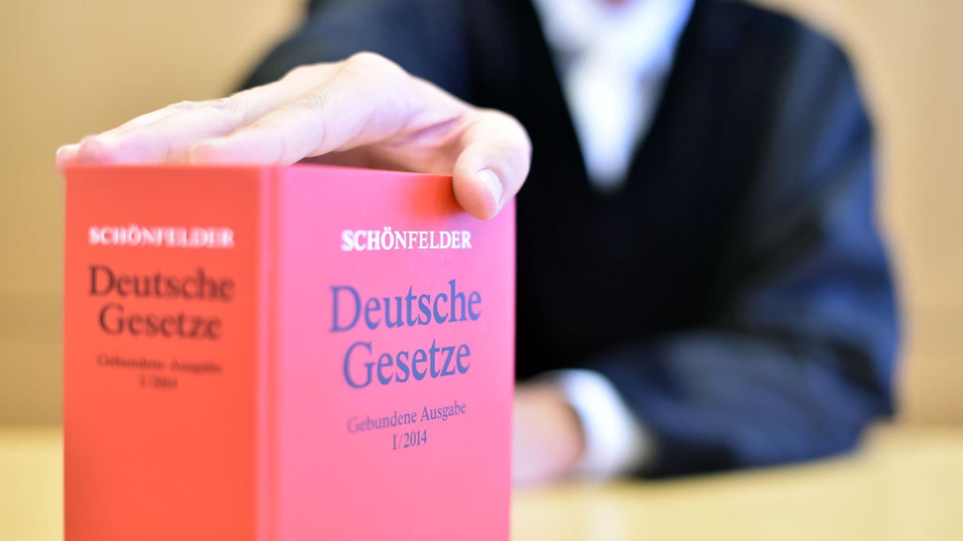 An der Richterbank eines Sitzungssaals sitzt ein Richter hinter einem Buch mit Deutschen Gesetzen.