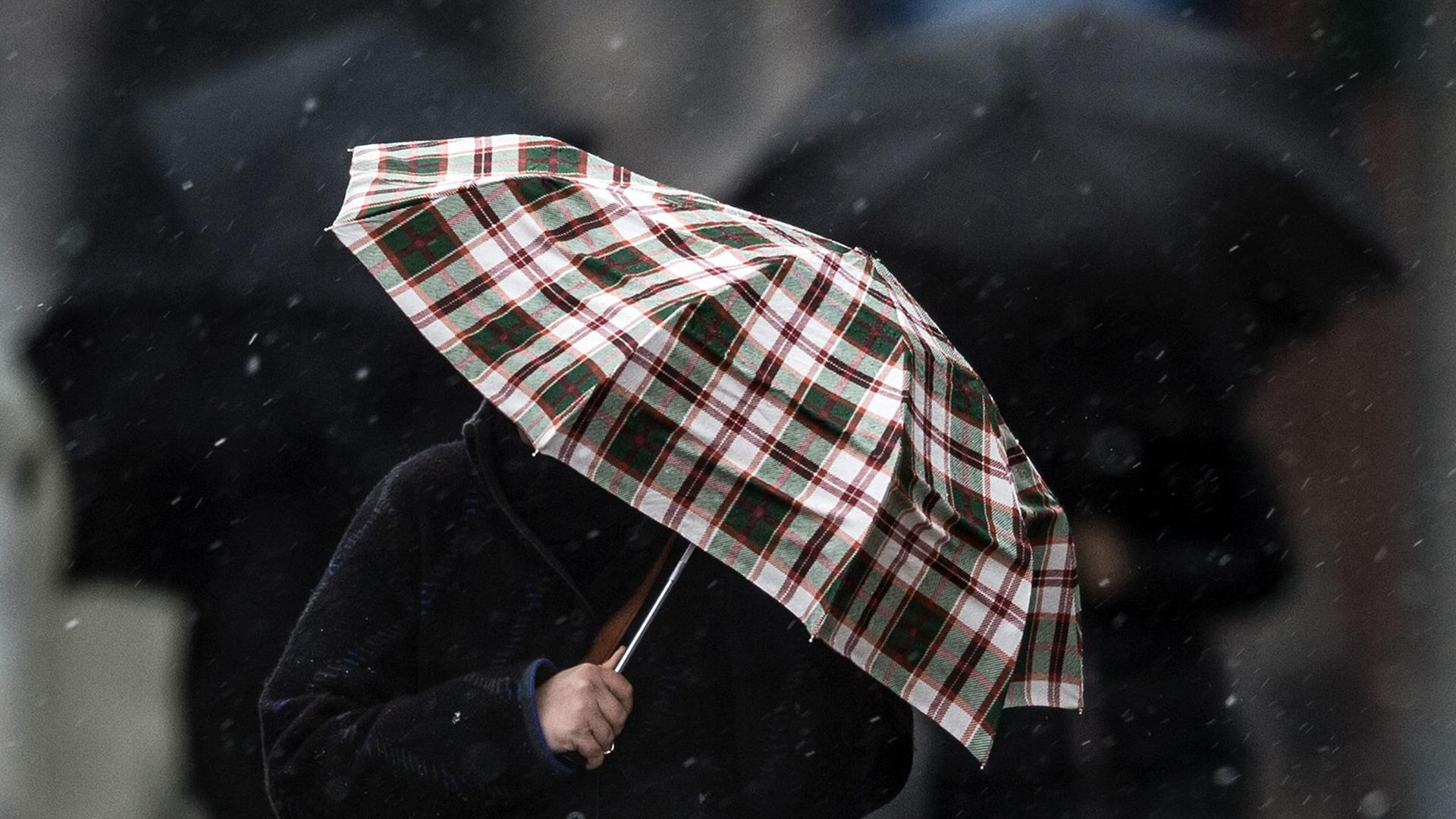 Fußgänger schützen sich mit Regenschirmen gegen den Schneeregen.