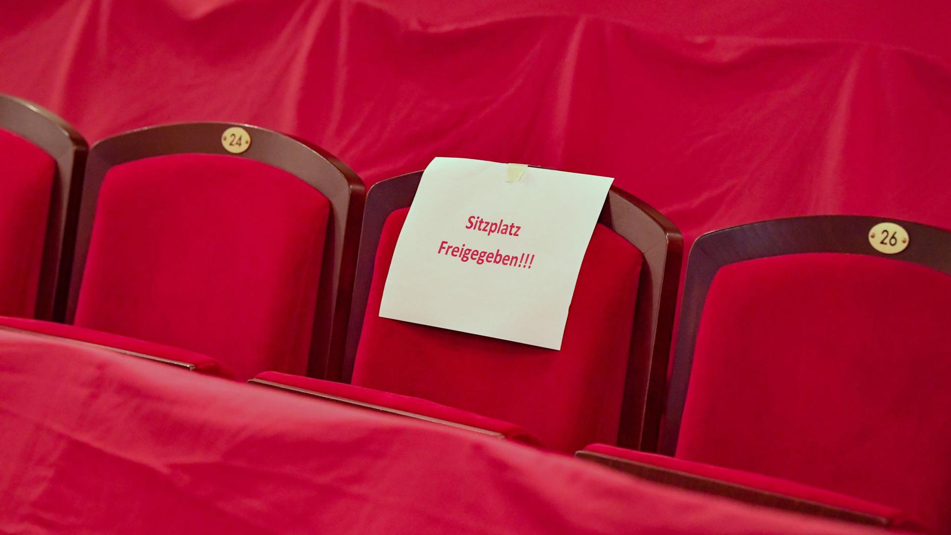 Ein Zettel mit der Aufschrift „Sitzplatz Freigegeben!!!“ hängt an einem Sitzplatz im leeren Zuschauerraum eines Theaters.