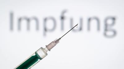 Eine Spritze wird vor den Schriftzug „Impfung“ gehalten.