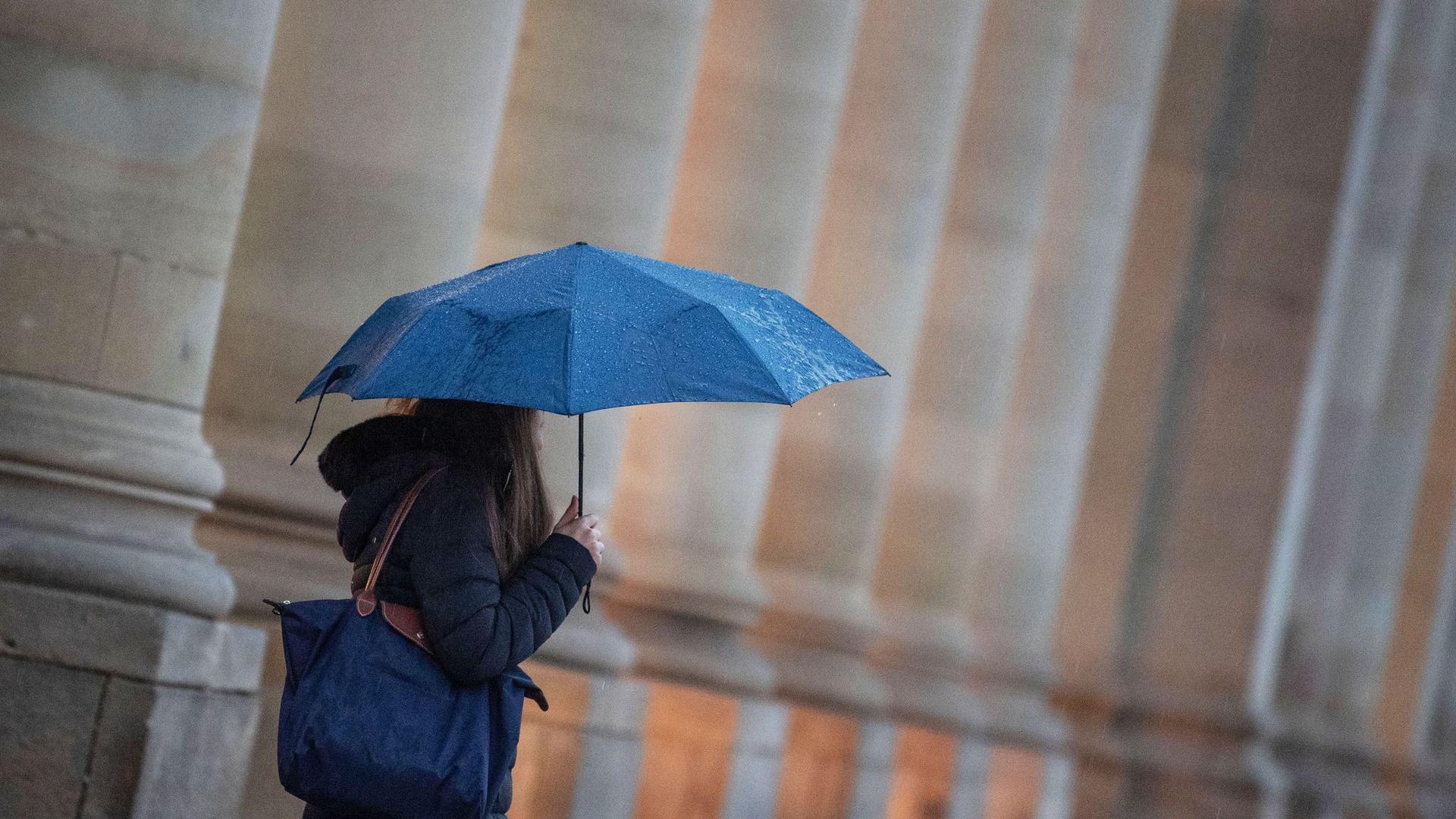 Eine Passantin geht bei Regen durch die Stadt.