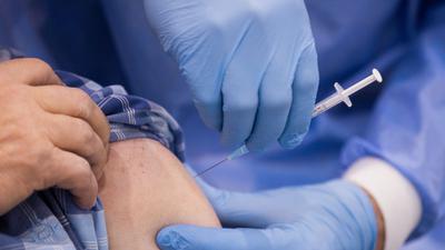 Ein Arzt impft einen Mann in einem Impfzentrum gegen Corona.